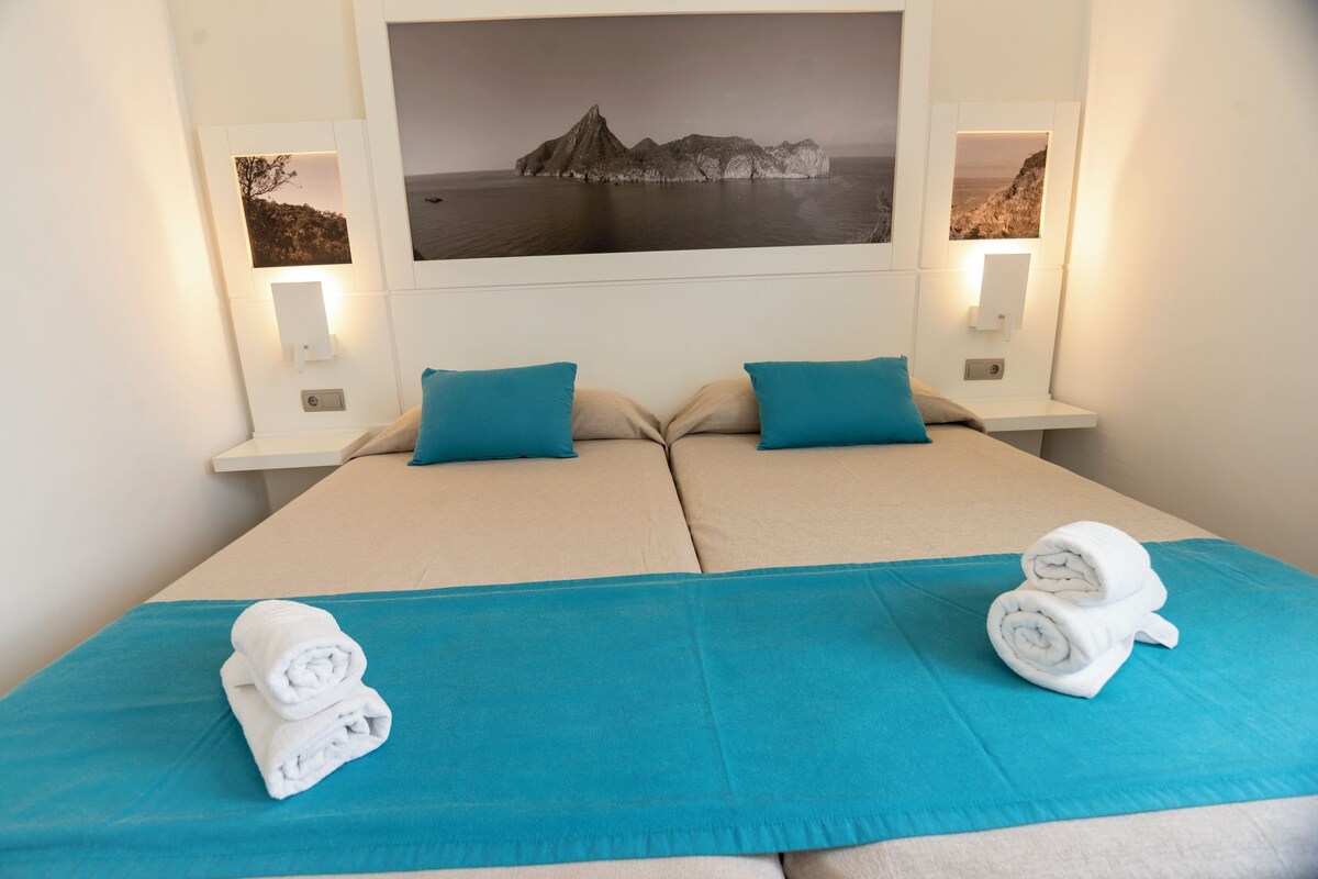 Ein Doppelbett mit zwei Kissen, einer blauen Bettdecke und zwei aufgerollten Handtüchern.