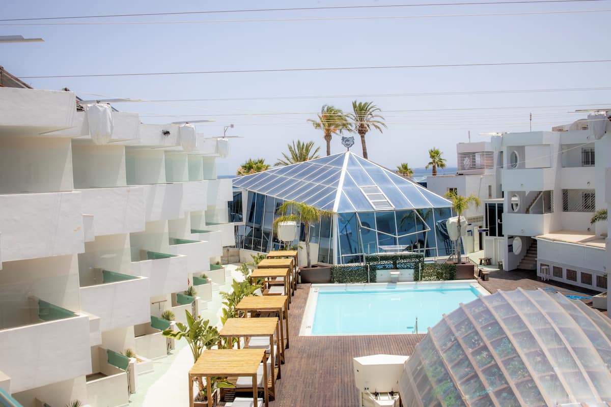 Un área de piscina en la azotea con una estructura de cristal, sillas de descanso y vistas despejadas de los edificios circundantes.