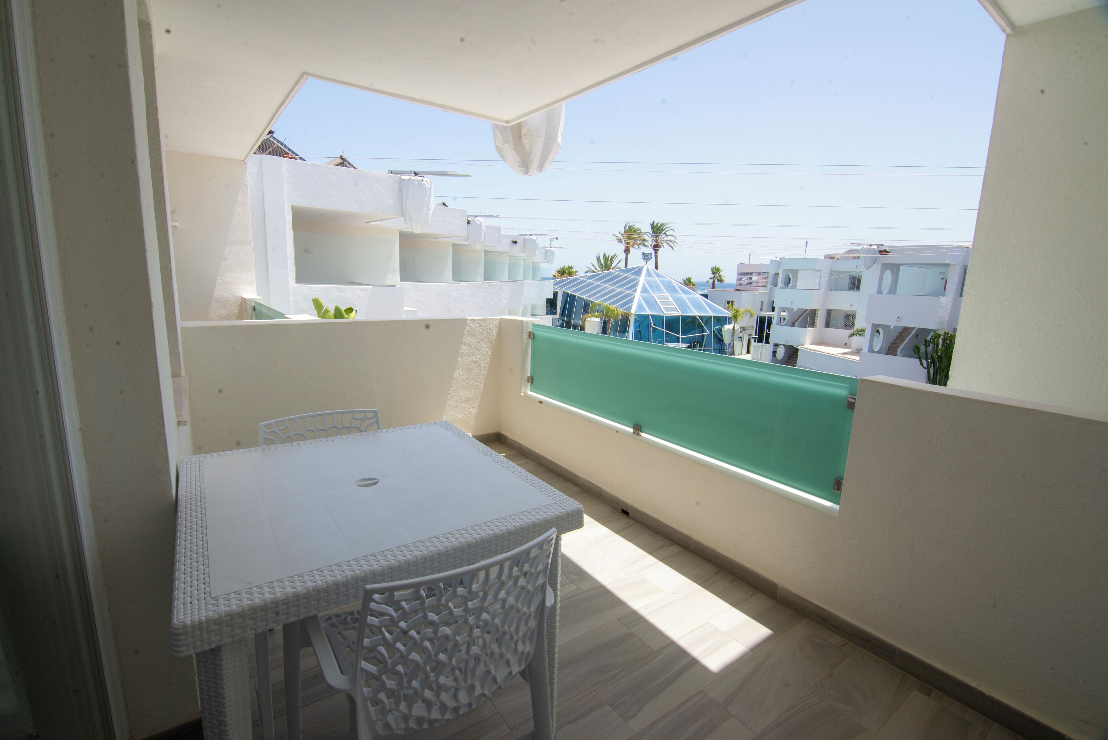 A balcony with a table and chairs, a view of buildings, and a clear sky.