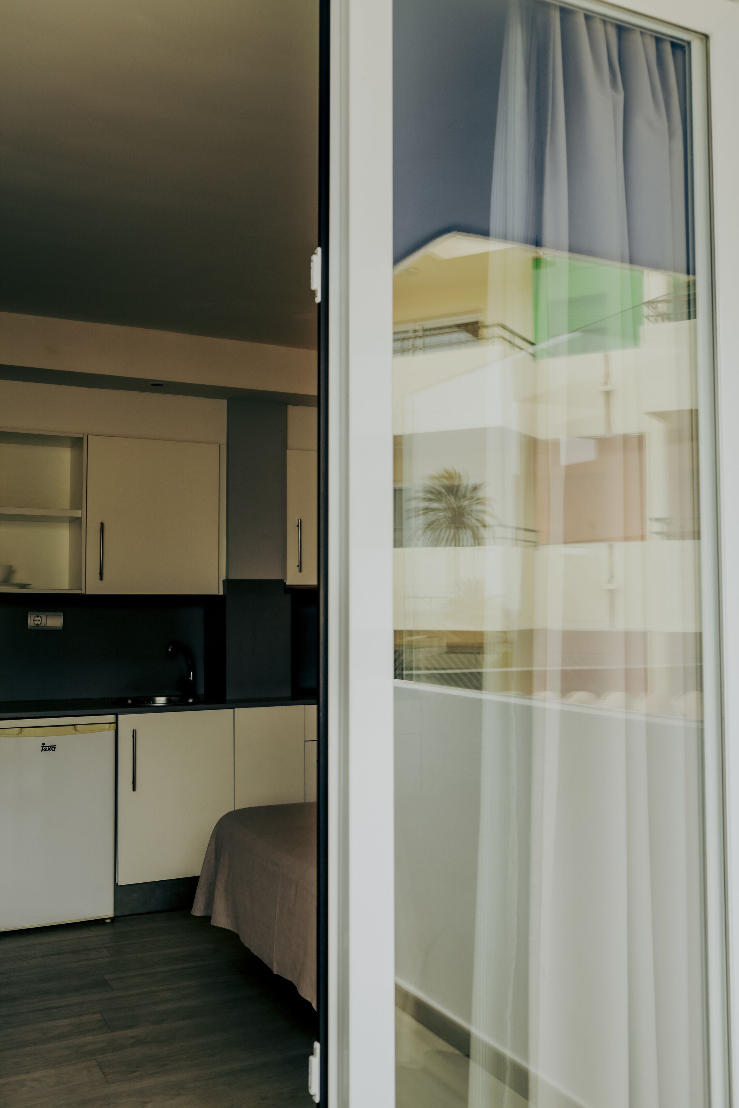 A modern kitchen with white cabinets, a black countertop, and a bed with a brown blanket.