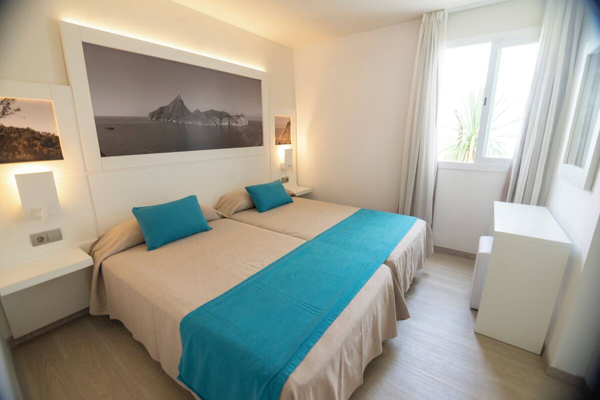 Habitación de hotel con dos camas, un cuadro grande enmarcado en la pared y una ventana con cortinas.