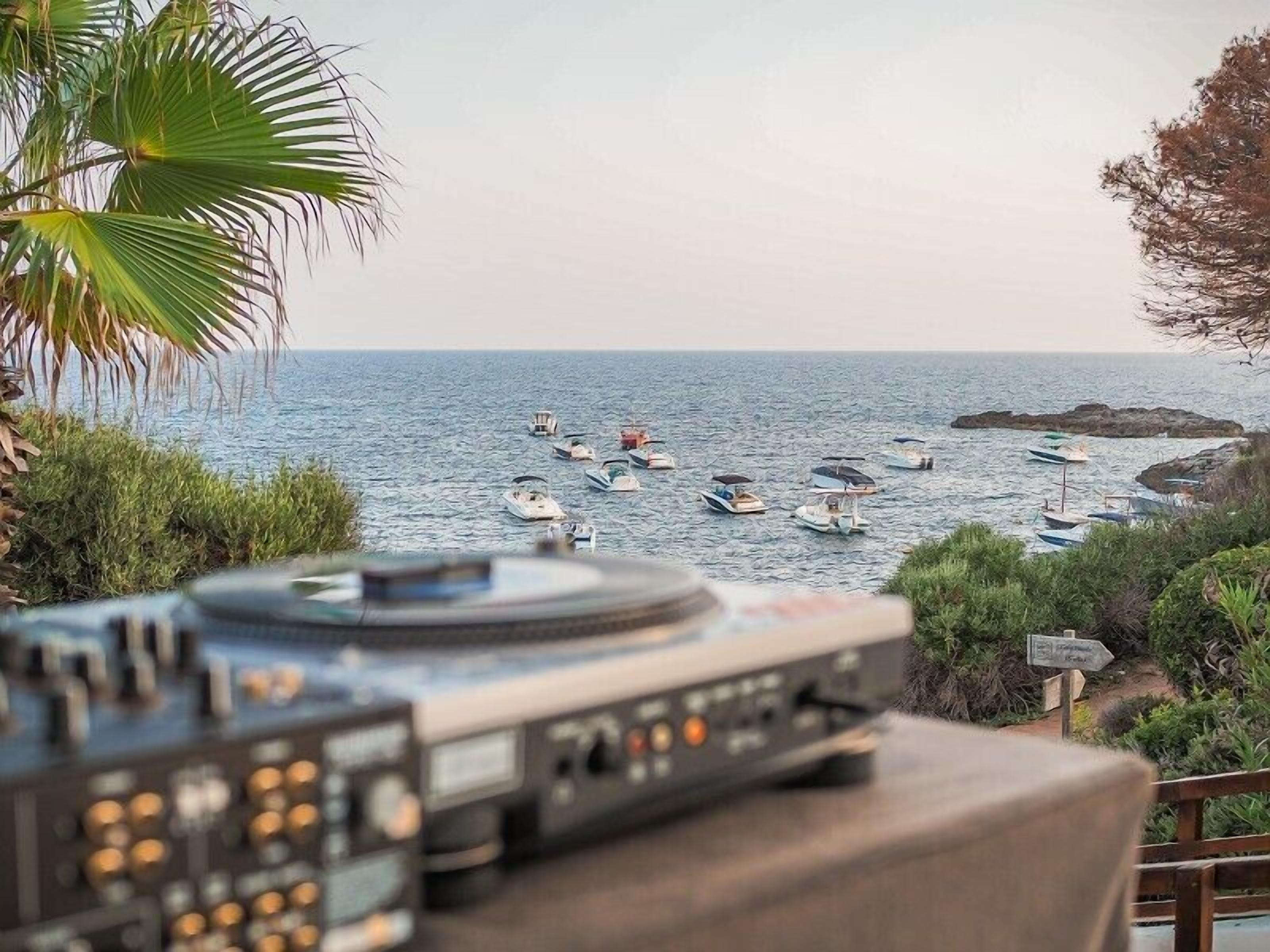 A DJ equipment setup overlooking a coastal area with boats and greenery.