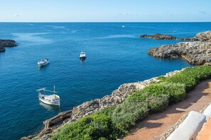 Un paysage côtier avec un terrain rocheux, une mer bleue et limpide, et des bateaux ancrés près du rivage.