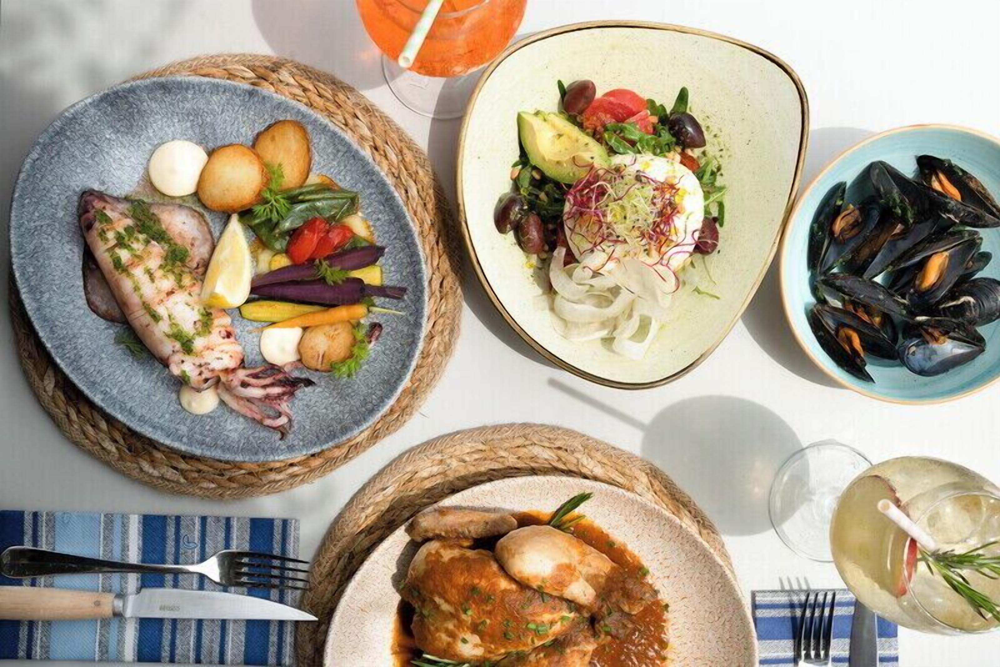 A table with various dishes including seafood, vegetables, and a drink.