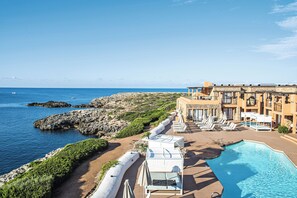 Un complexe hôtelier doté d’une piscine, de chaises longues et offrant une vue sur la mer.