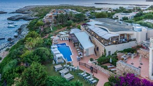 A coastal resort with a swimming pool, outdoor seating, and a view of the sea. - Hotel Menorca Binibeca  - Adults Recommended- by Pierre & Vacances Premium (Sant Lluis)
