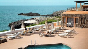 A poolside area with lounge chairs and umbrellas, overlooking the sea. - Hotel Menorca Binibeca  - Adults Recommended- by Pierre & Vacances Premium (Sant Lluis)