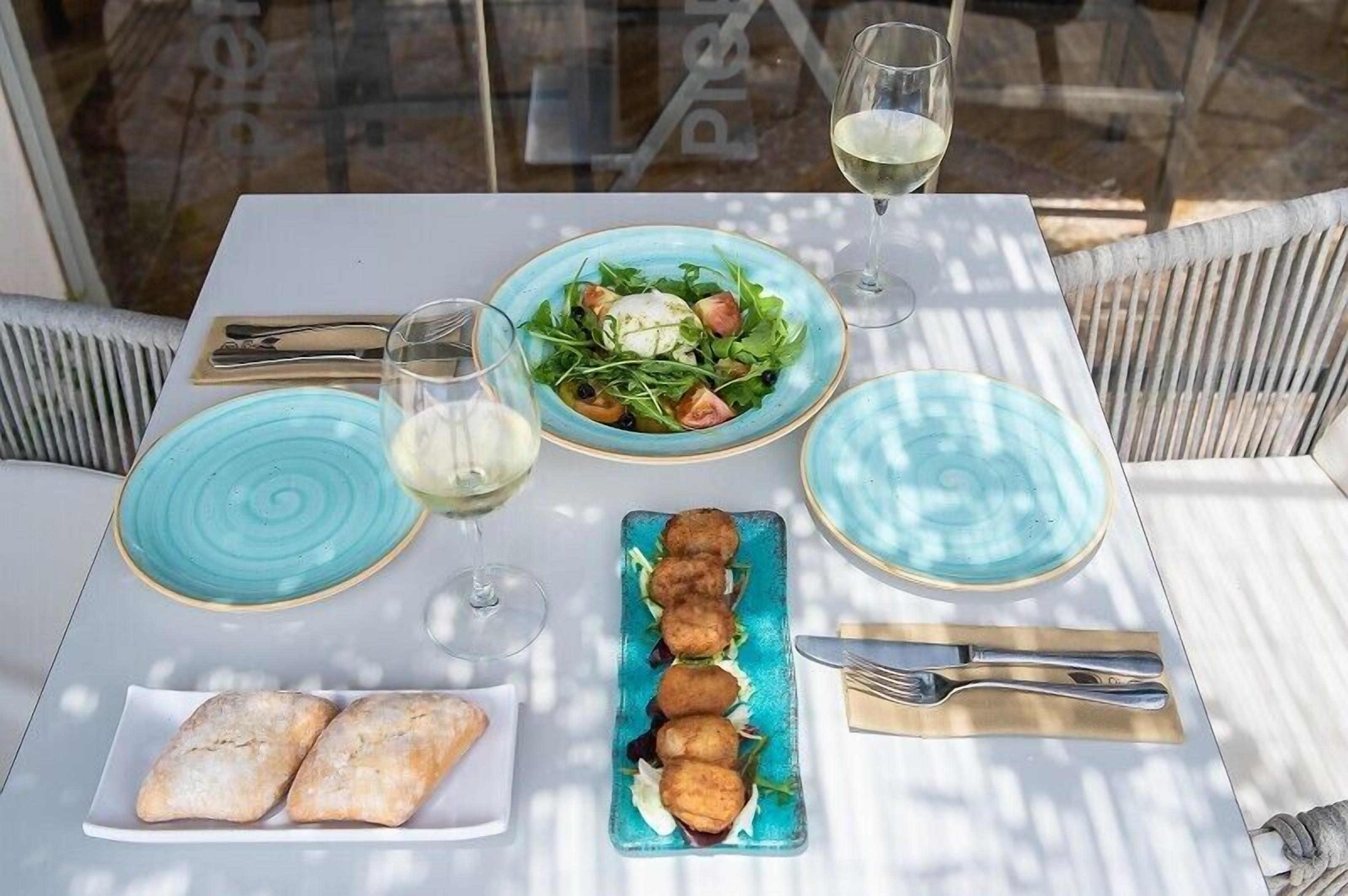Ein Tisch, reichhaltig gedeckt mit Salat, Kroketten und Brot, dazu Weingläser.
