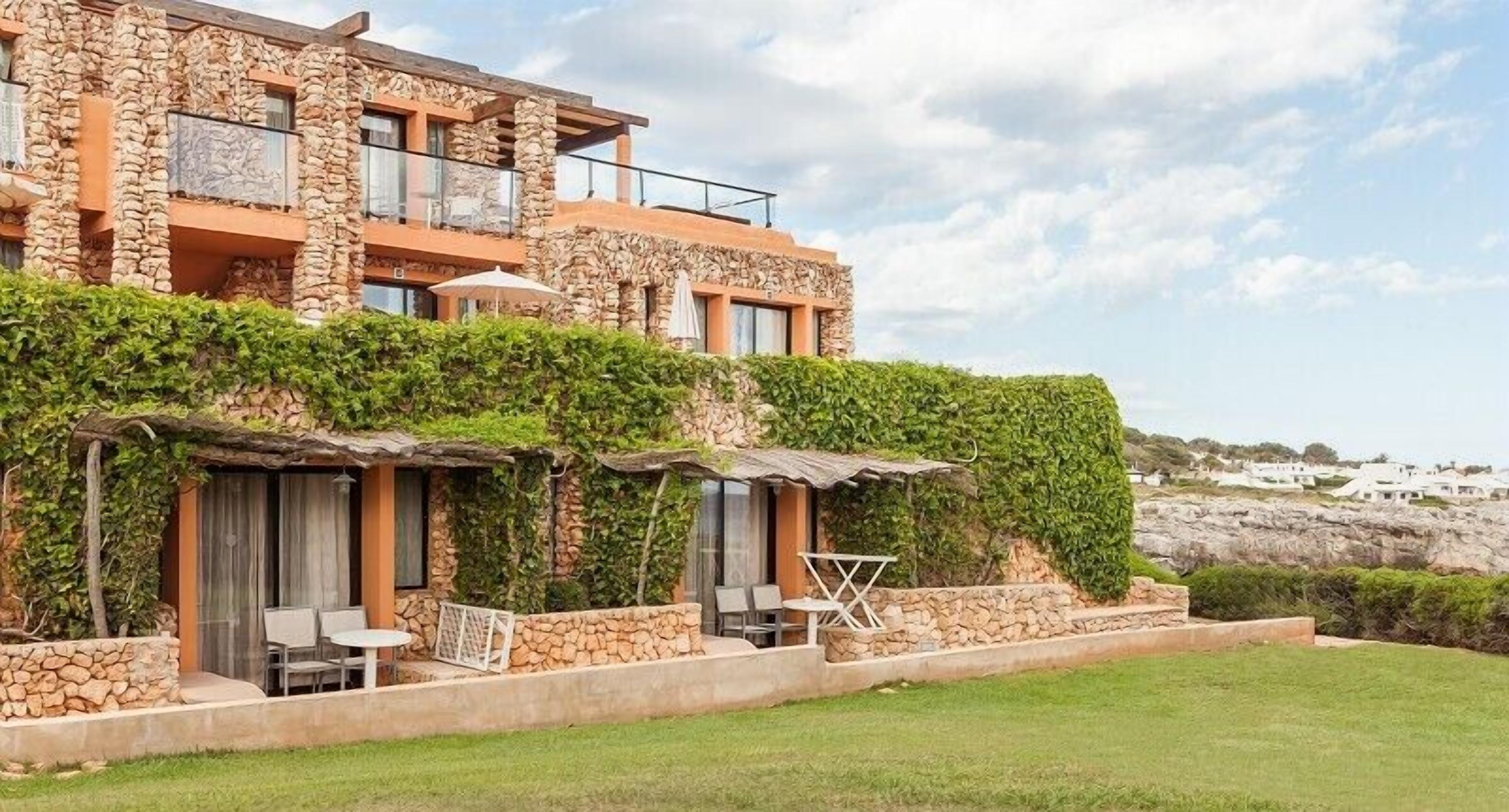 A multi-story stone building with outdoor seating and a view of the sea.