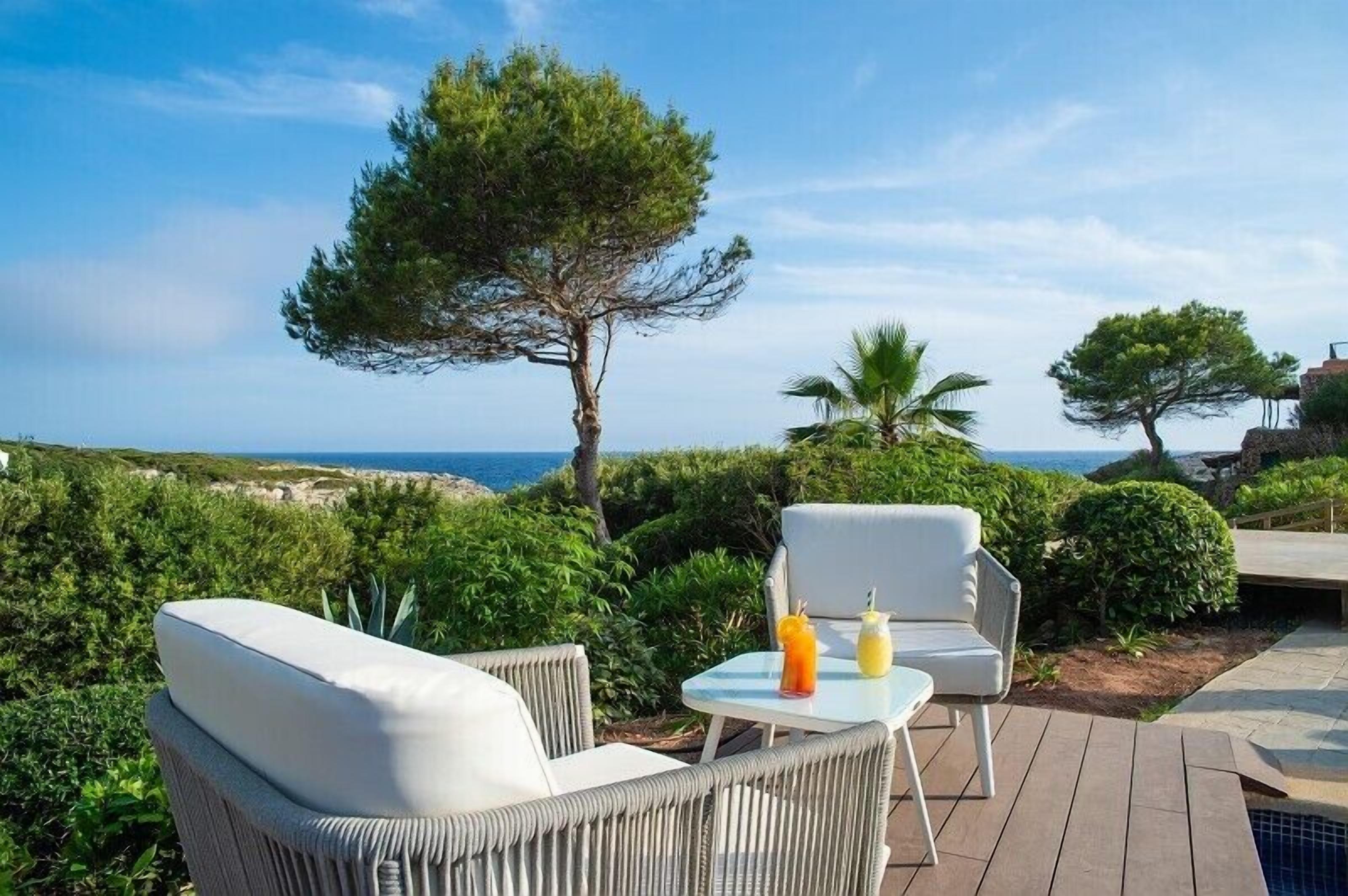 A patio with wicker furniture and a table, overlooking a scenic coastal view.