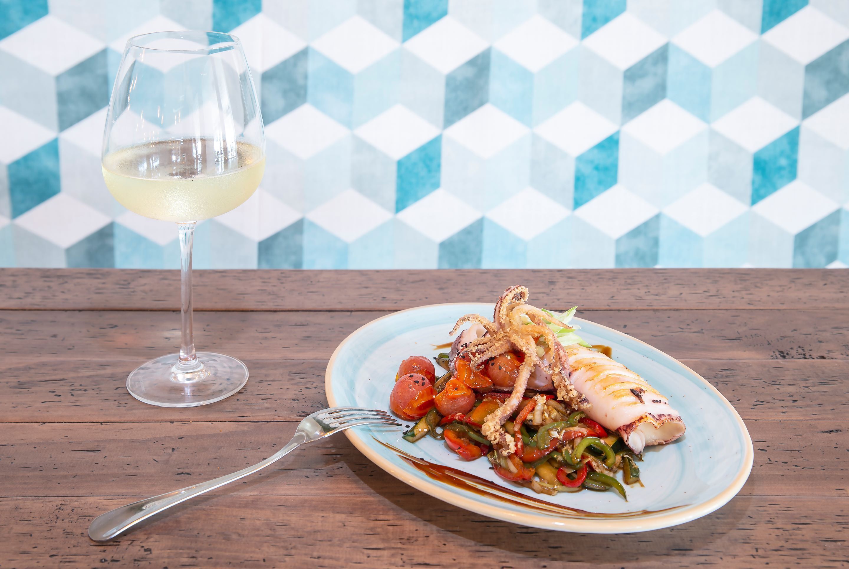 A plate of food with a glass of white wine on a wooden table.