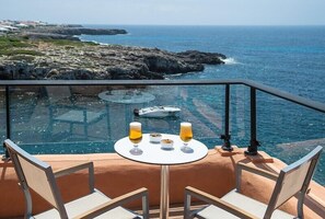 Un área de comedor al aire libre con paredes de vidrio, con una mesa dispuesta para dos personas, con vistas a un litoral rocoso y al mar.