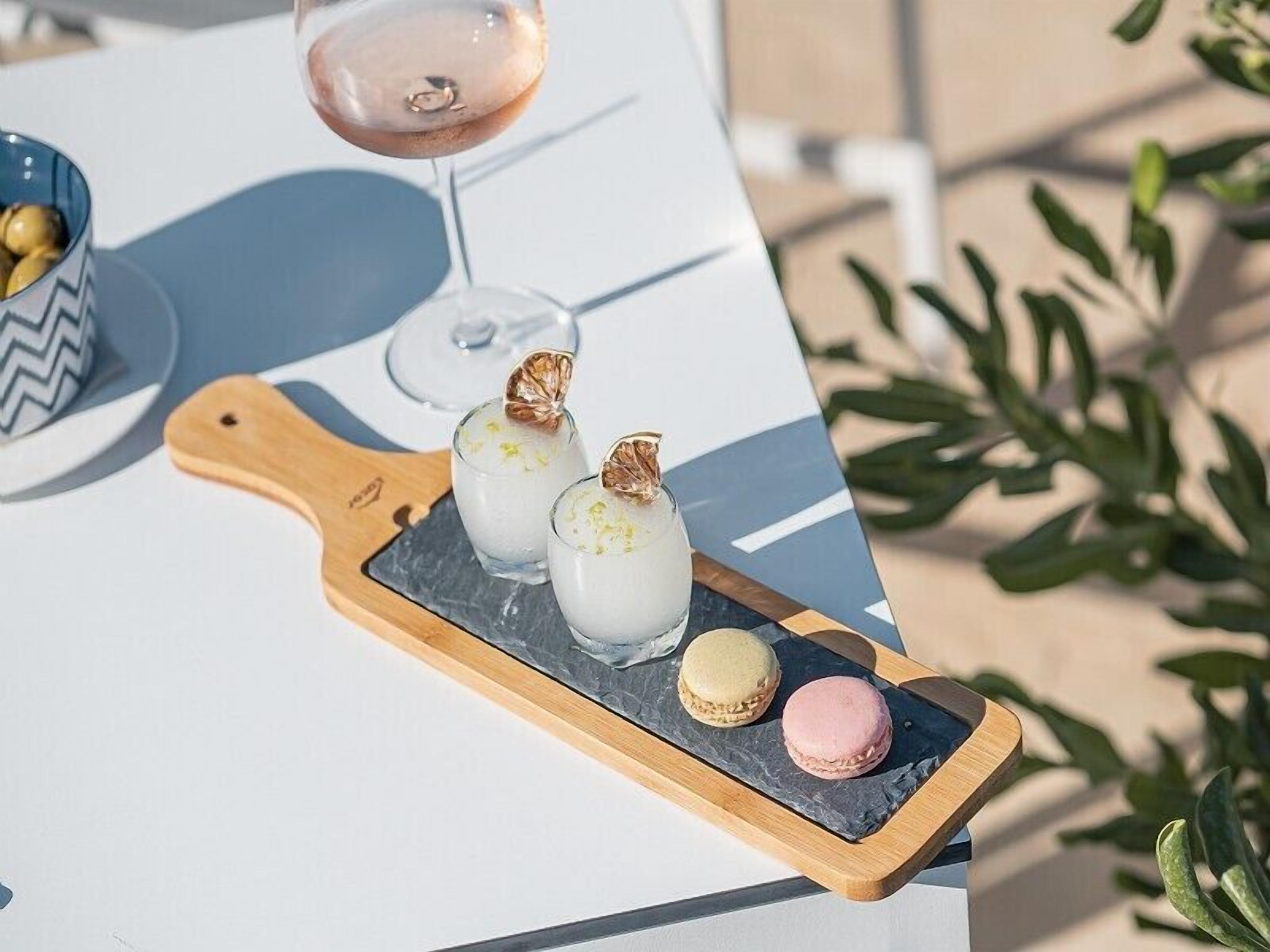 Een plateau met macarons en een glas roze drank op een tafel.
