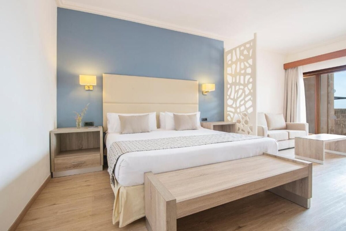 Ein modernes Hotelzimmer mit einem großen Bett, Nachttischen, einer Sitzecke und Balkonblick.