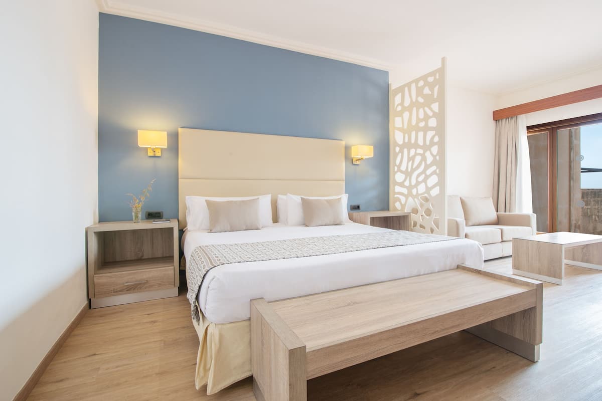 Une chambre d’hôtel moderne avec un grand lit, des tables de chevet, un canapé et un balcon avec vue.