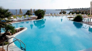 A clear blue pool with white lounge chairs and umbrellas, surrounded by greenery and overlooking the sea. - Grupotel Tamariscos (Ciutadella de Menorca)