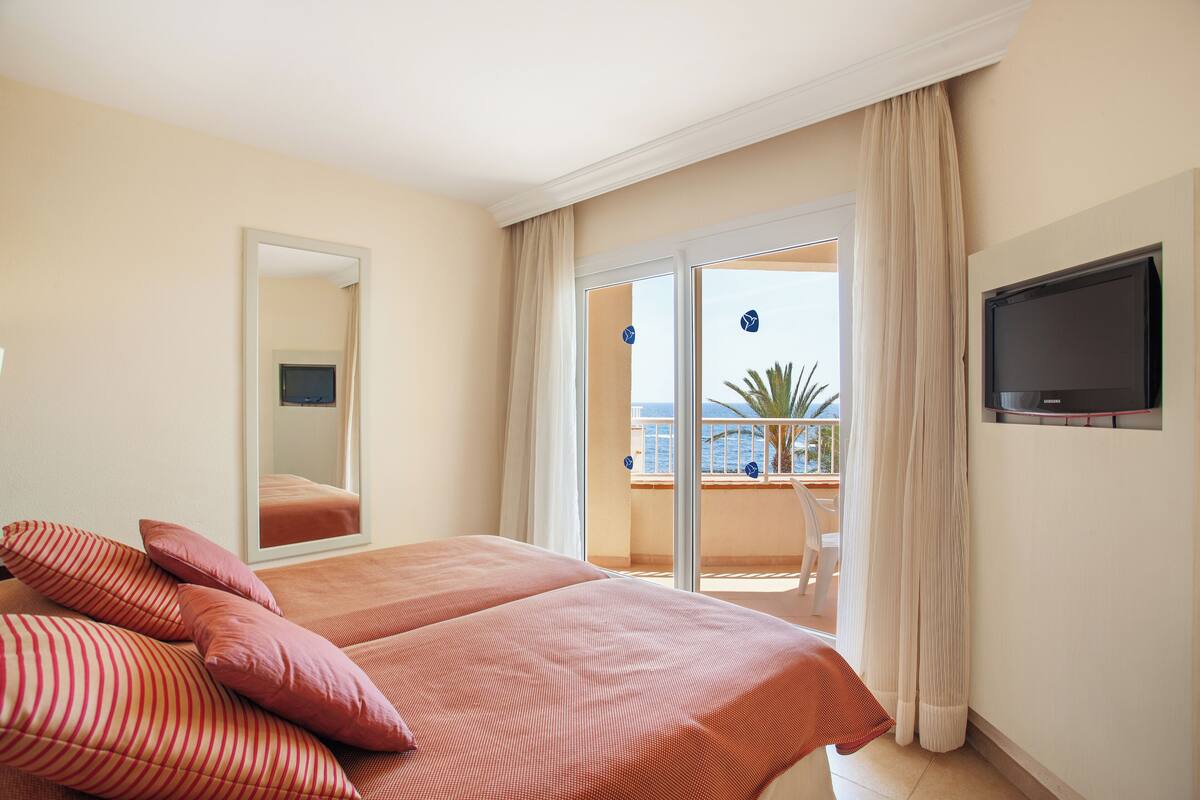 Une chambre d  ’hôtel avec un lit, une télévision et un balcon donnant sur la mer.