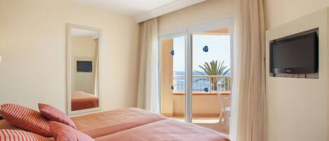 A hotel room with a bed, a TV, and a balcony with a view of the sea.
