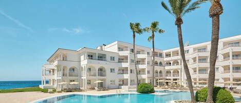 Un hotel con piscina, palmeras y vistas al mar.