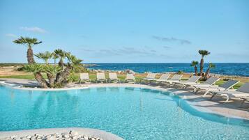 A clear blue pool with lounge chairs and palm trees, overlooking the ocean.
