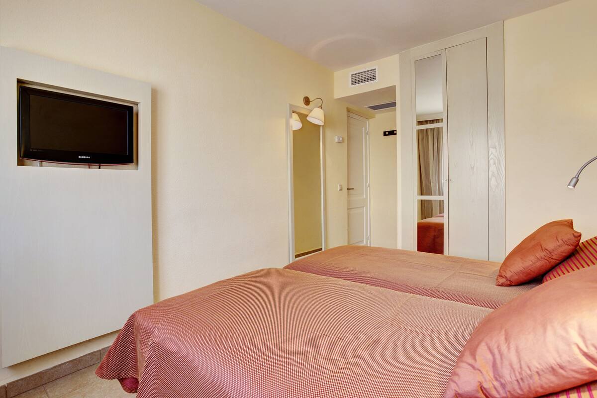 Une chambre avec deux lits, un téléviseur fixé au mur et une armoire avec un miroir.