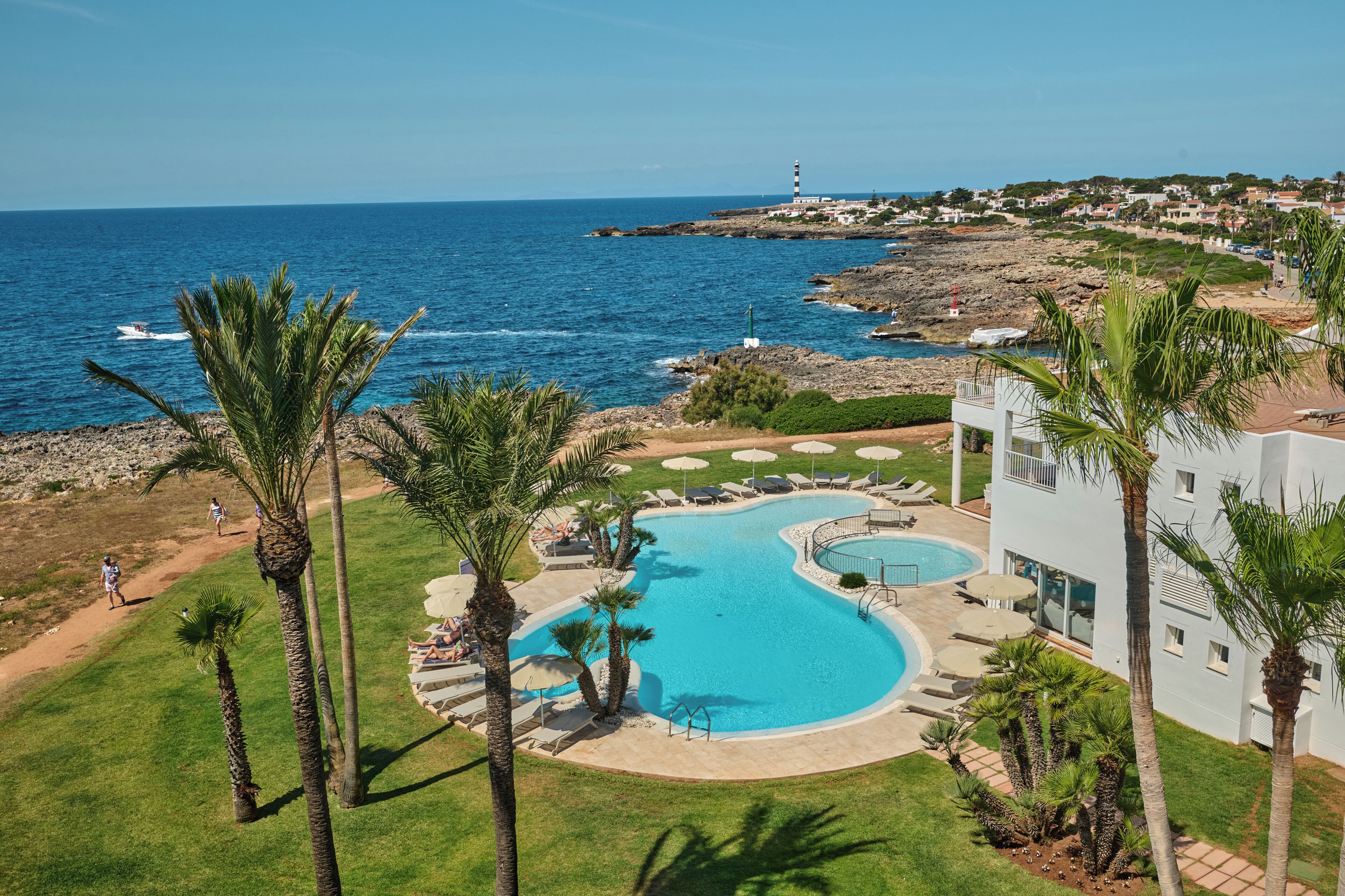 Et resort med en stor swimmingpool, palmer og havudsigt.