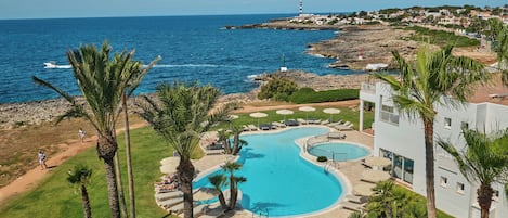 A resort with a large swimming pool, palm trees, and a view of the sea.