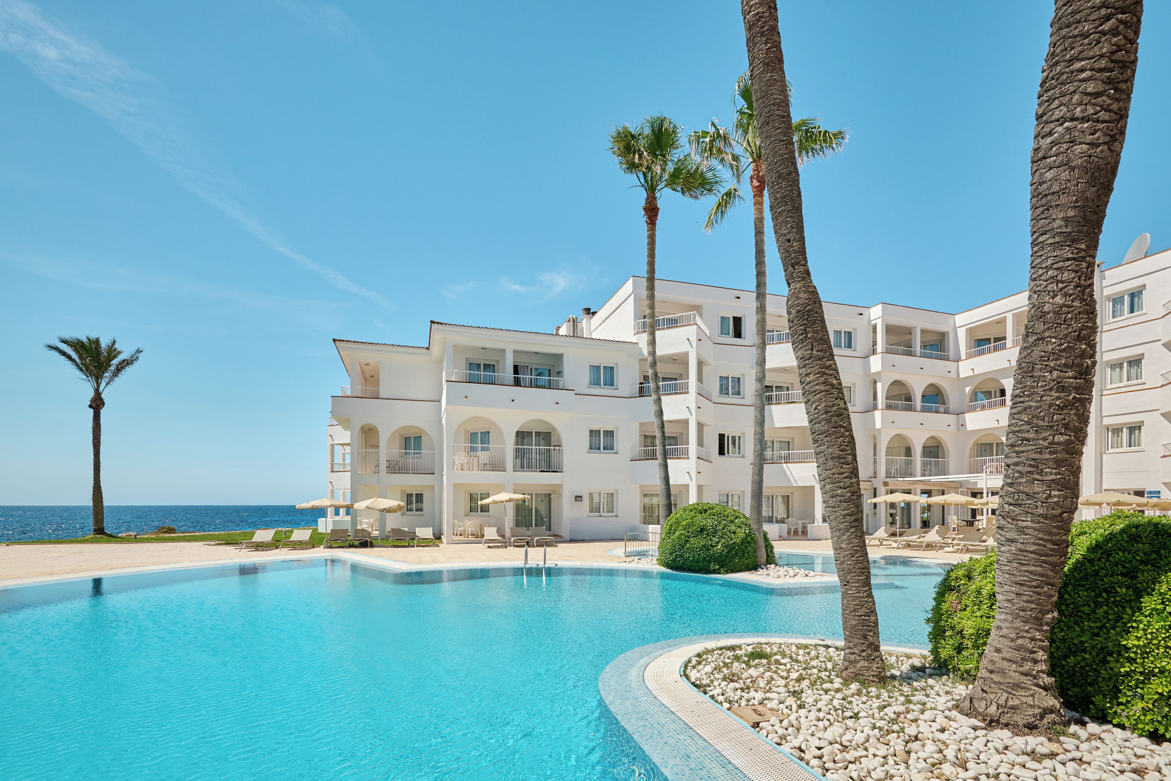 A resort with a pool, palm trees, and a view of the sea.