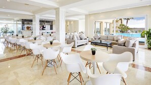 A spacious lobby with a pool view, modern furniture, and a bar area. - Grupotel Tamariscos (Ciutadella de Menorca)