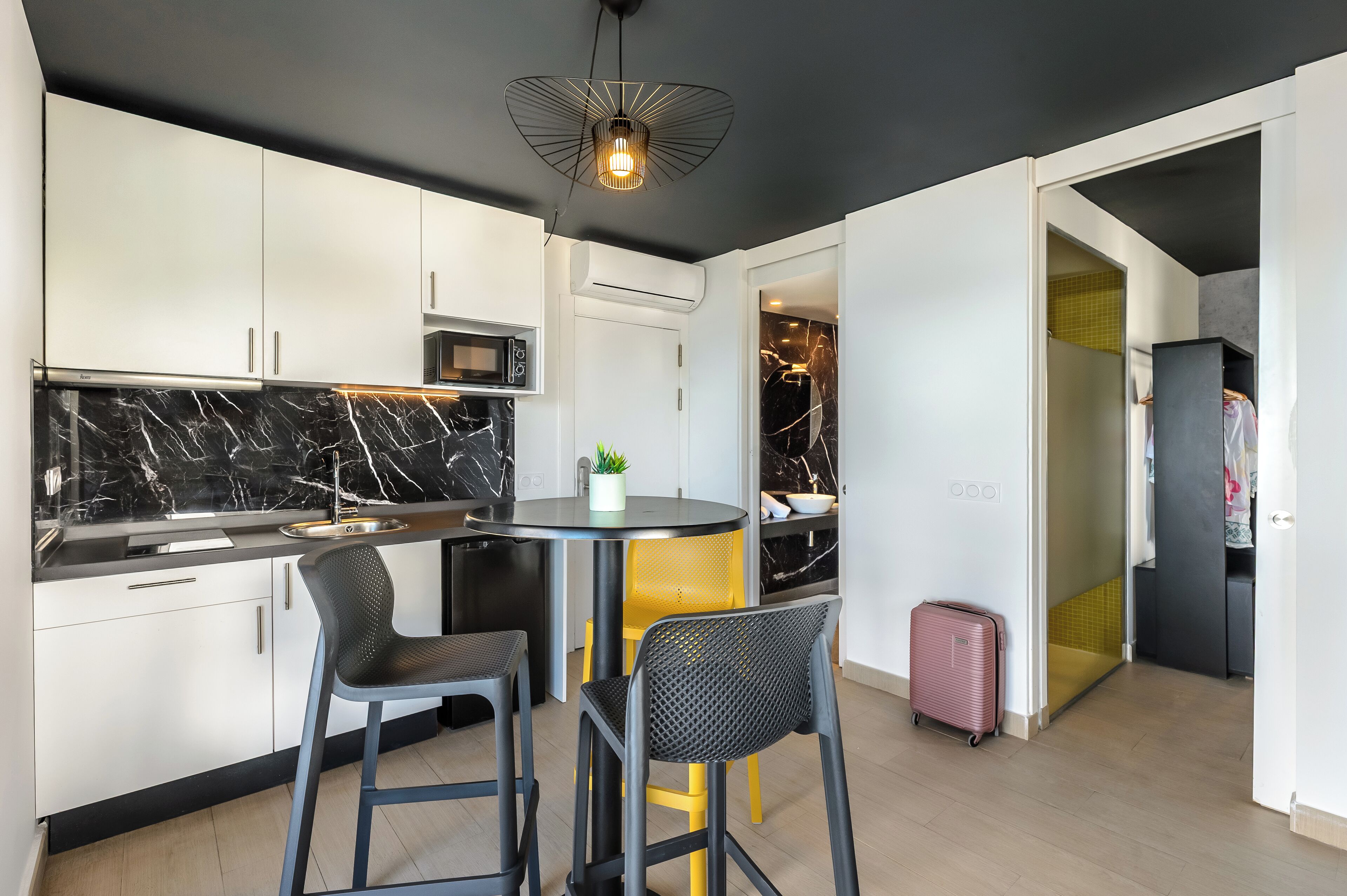 Una cocina moderna con armarios blancos, un salpicadero de mármol negro y una mesa redonda de comedor con dos sillas.