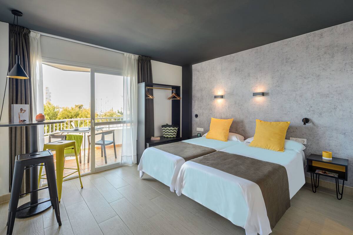 A modern hotel room with a large bed, a balcony with a table and chairs, and a view of the city.