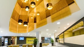 Un hall d’entrée moderne avec un plafond haut, de nombreuses suspensions sphériques et un espace détente avec des canapés et des plantes en pot.