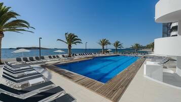 A pool area with lounge chairs and palm trees, overlooking the sea.