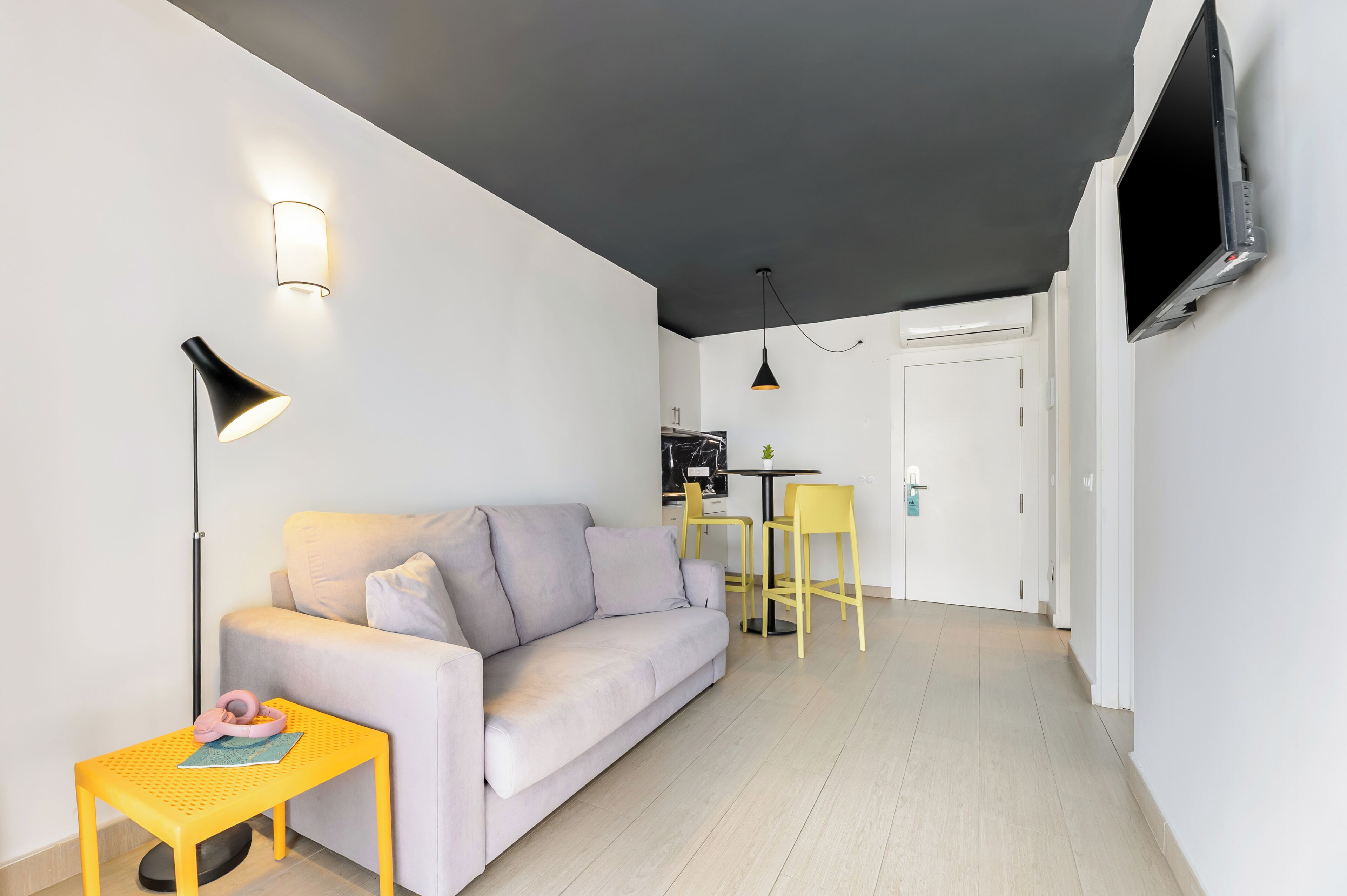 A modern living room with a sofa, a small table, a TV, and a dining area with chairs.