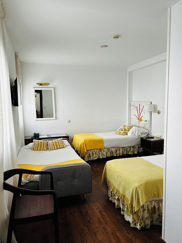 Habitación de hotel con dos camas individuales, un escritorio, una silla, un espejo, una lámpara y una luz de techo.