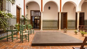 Un patio con piso de baldosas, sillas verdes y plantas en macetas.