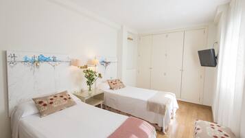 A hotel room with two beds, a TV mounted on the wall, and a wardrobe.