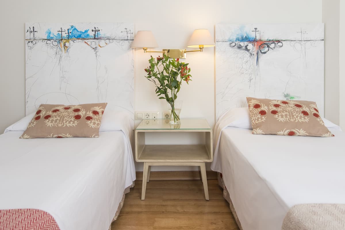 A hotel room with two beds, a small table with a vase of flowers, and wall art above the bed.