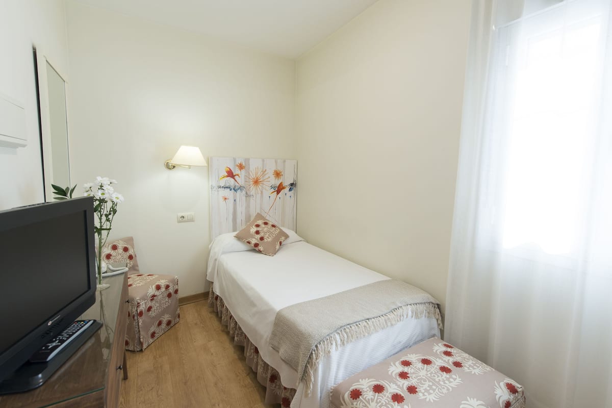A small, neatly arranged bedroom with a bed, bedside table, and a television.