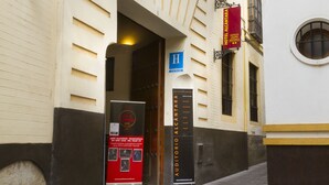 Una calle estrecha con un edificio que tiene una puerta de madera grande, un letrero rojo y un letrero azul.