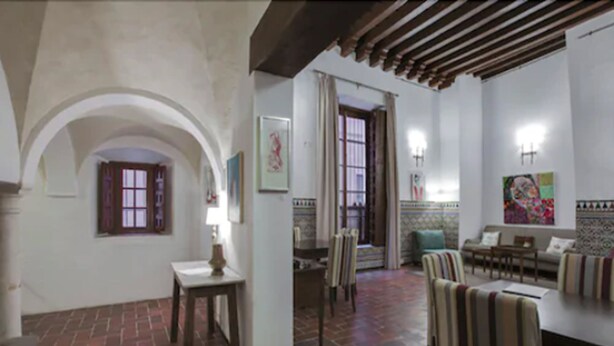 Amplia sala de estar con piso de ladrillo, comedor con sillas a rayas y un rincón de estar acogedor con sofá y cojines.