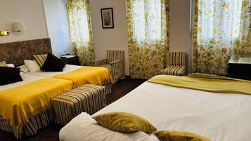 A hotel room with two beds, striped chairs, a small table, and floral curtains.