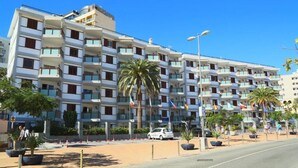 A multi-story hotel with balconies, palm trees, and flags. - Apartamentos Las Góndolas (San Bartolomé de Tirajana)
