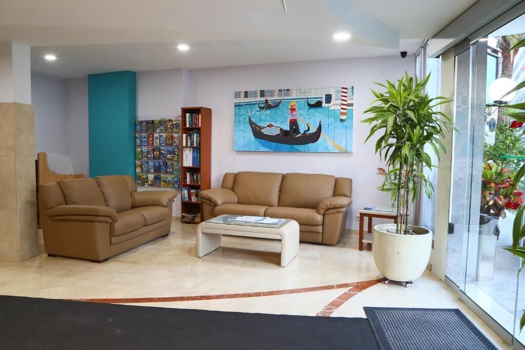 Un salon moderne avec deux canapés marron, une table basse, une bibliothèque et un grand tableau représentant une gondole, accroché au mur.