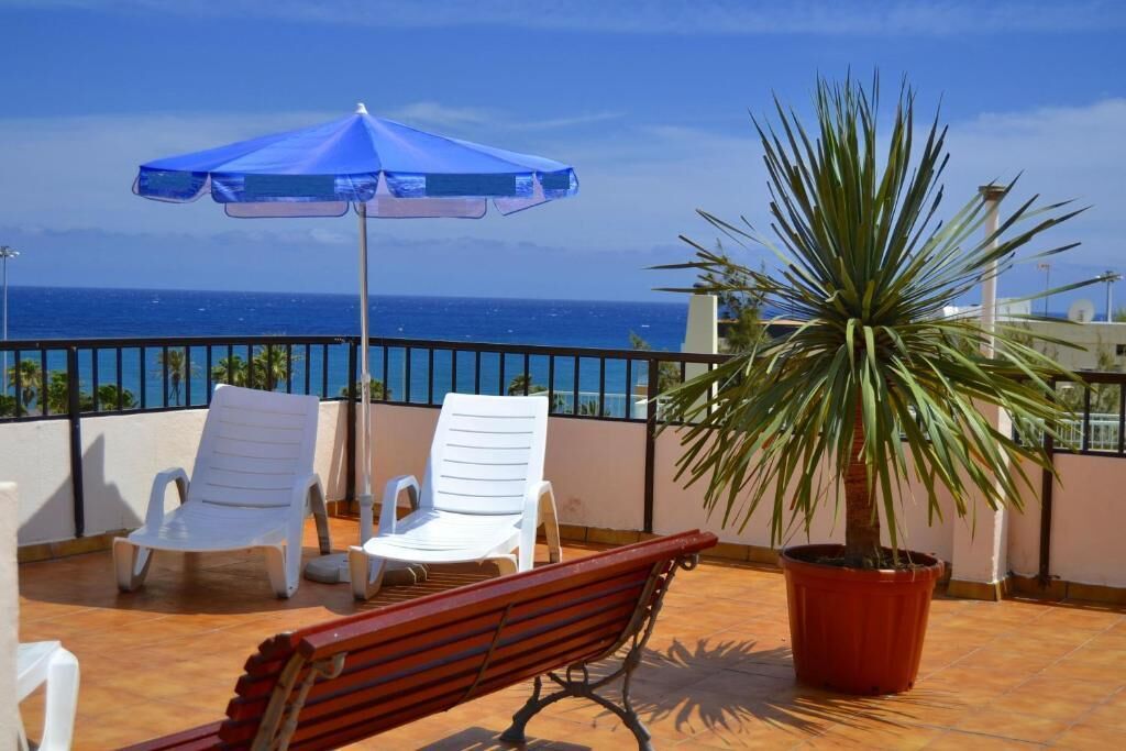 A terrace with white chairs, a blue umbrella, and a potted plant.