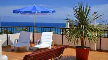 A terrace with white chairs, a blue umbrella, and a potted plant.