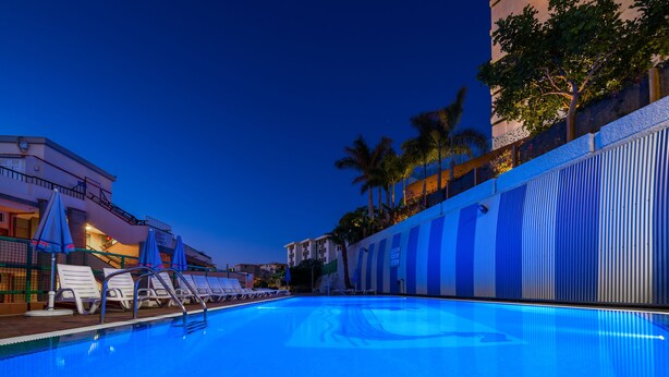 A swimming pool with lounge chairs and umbrellas, surrounded by buildings and palm trees. - Apartamentos Las Góndolas (San Bartolomé de Tirajana)
