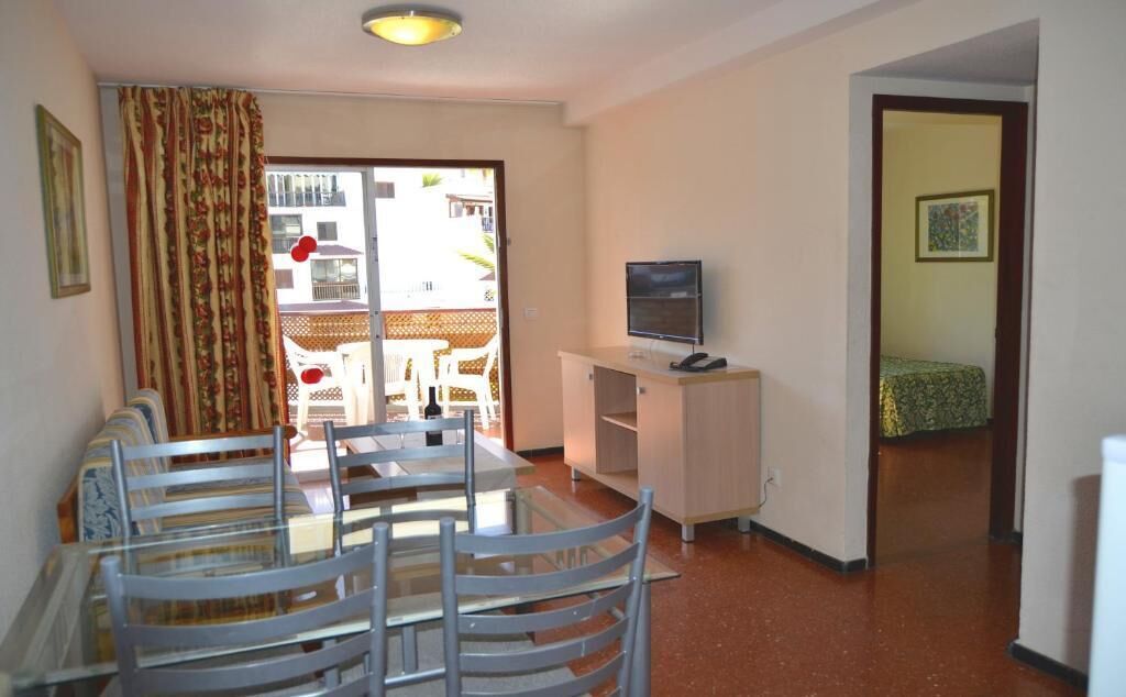 A compact living space with a dining area, a television, and a balcony with a view.