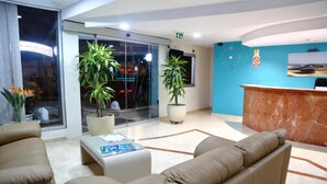 A hotel lobby with a reception desk, seating area, and large windows. - Apartamentos Las Góndolas (San Bartolomé de Tirajana)