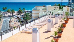 A rooftop terrace with sun loungers and potted plants, overlooking a beach and the ocean. - Apartamentos Las Góndolas (San Bartolomé de Tirajana)